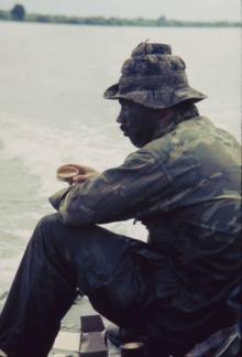 SEAL Team One member Clarke Long eats C-Rations on the stern of a landing craft cruising the Bassac River.