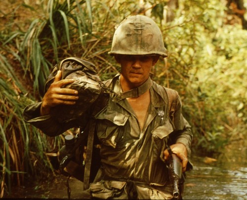 A medic of the 9th Infantry Division holds his rubberized M3 Aid Bag clear of the water whilst wading through a stream.