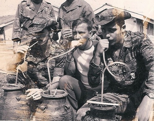 Special Mission Force (SMF) members Ferricks, Brown and Curtis (left to right) drink rice wine at a Montagnard party.