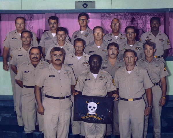 In their only in-country team photo, US members of the Special Mission Force stand under the porch outside the bar at the old 5th SFG C-Team compound in Pleiku, II CTZ.